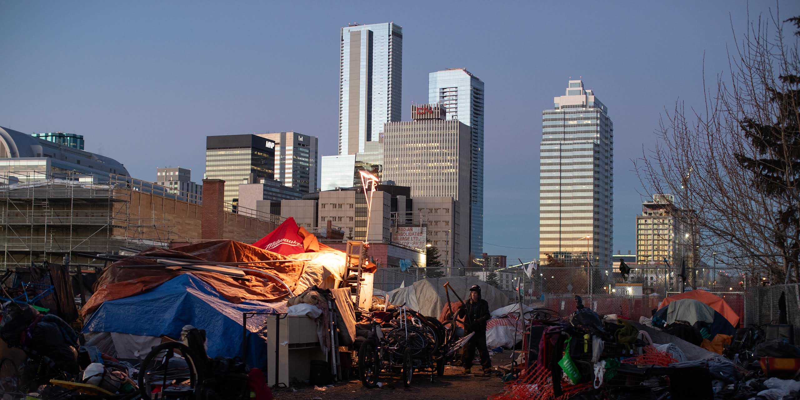 Tents at an encampment, tall glass buildings in the background