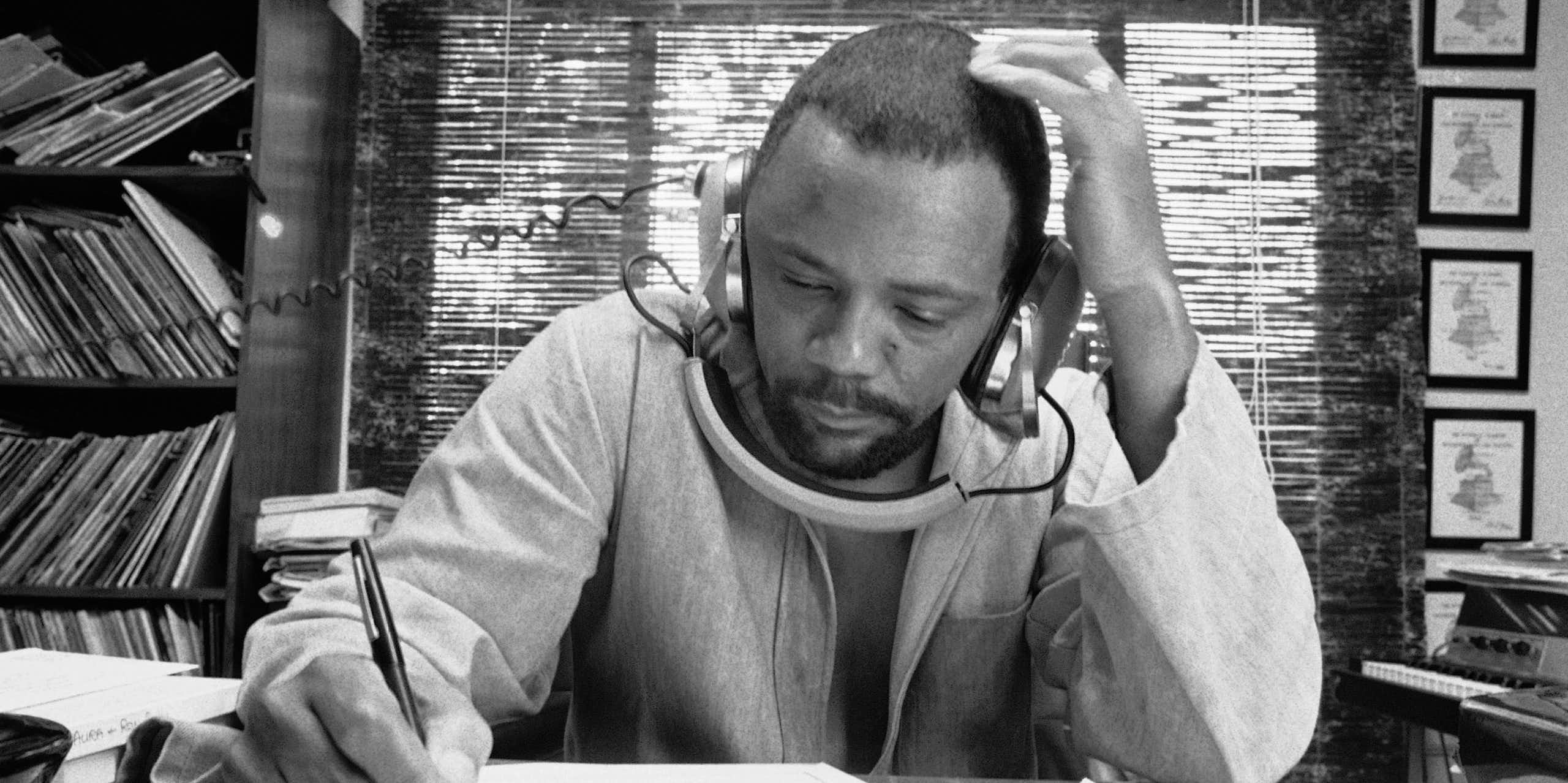 A man writing music, listening to a recording on his headphones