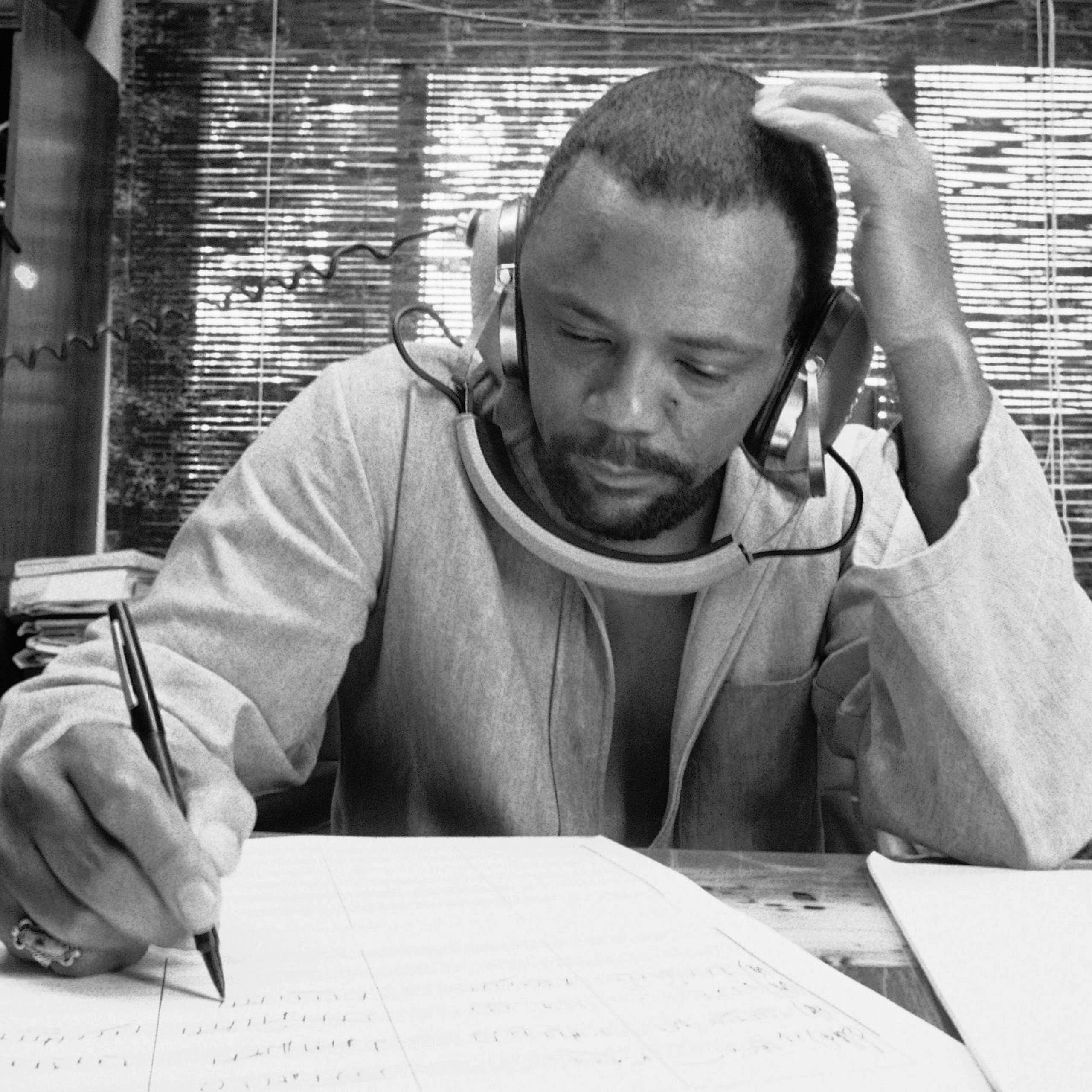 A man writing music, listening to a recording on his headphones