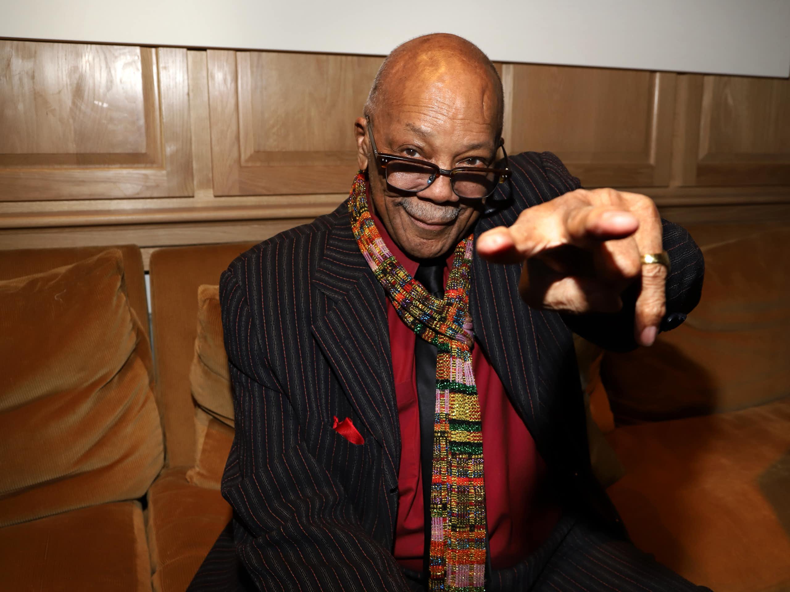 Bald black man wearing glasses points at a camera and grins.