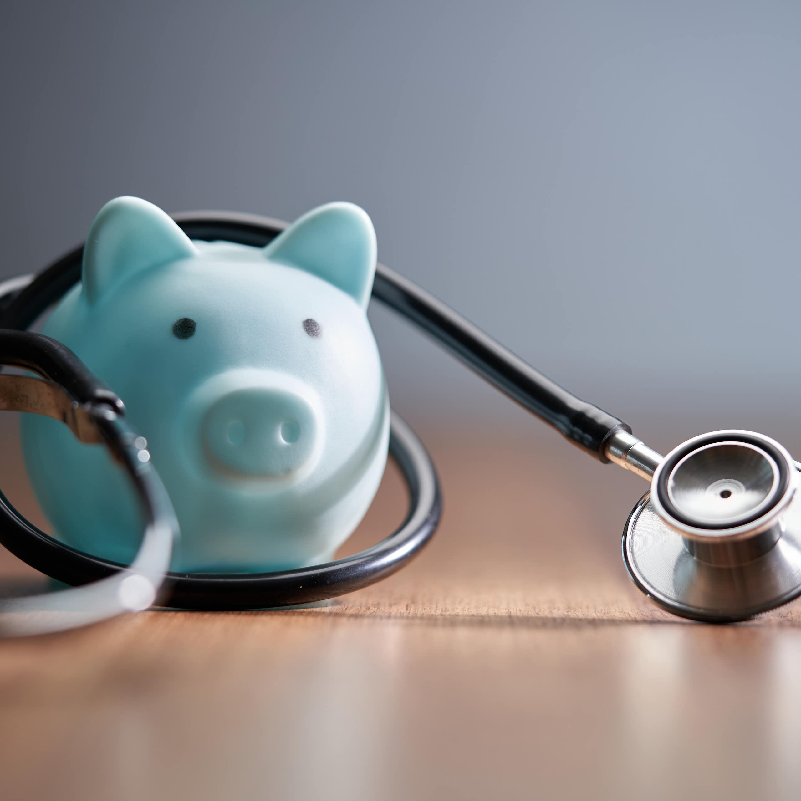 stethoscope and blue piggy bank on wood table top