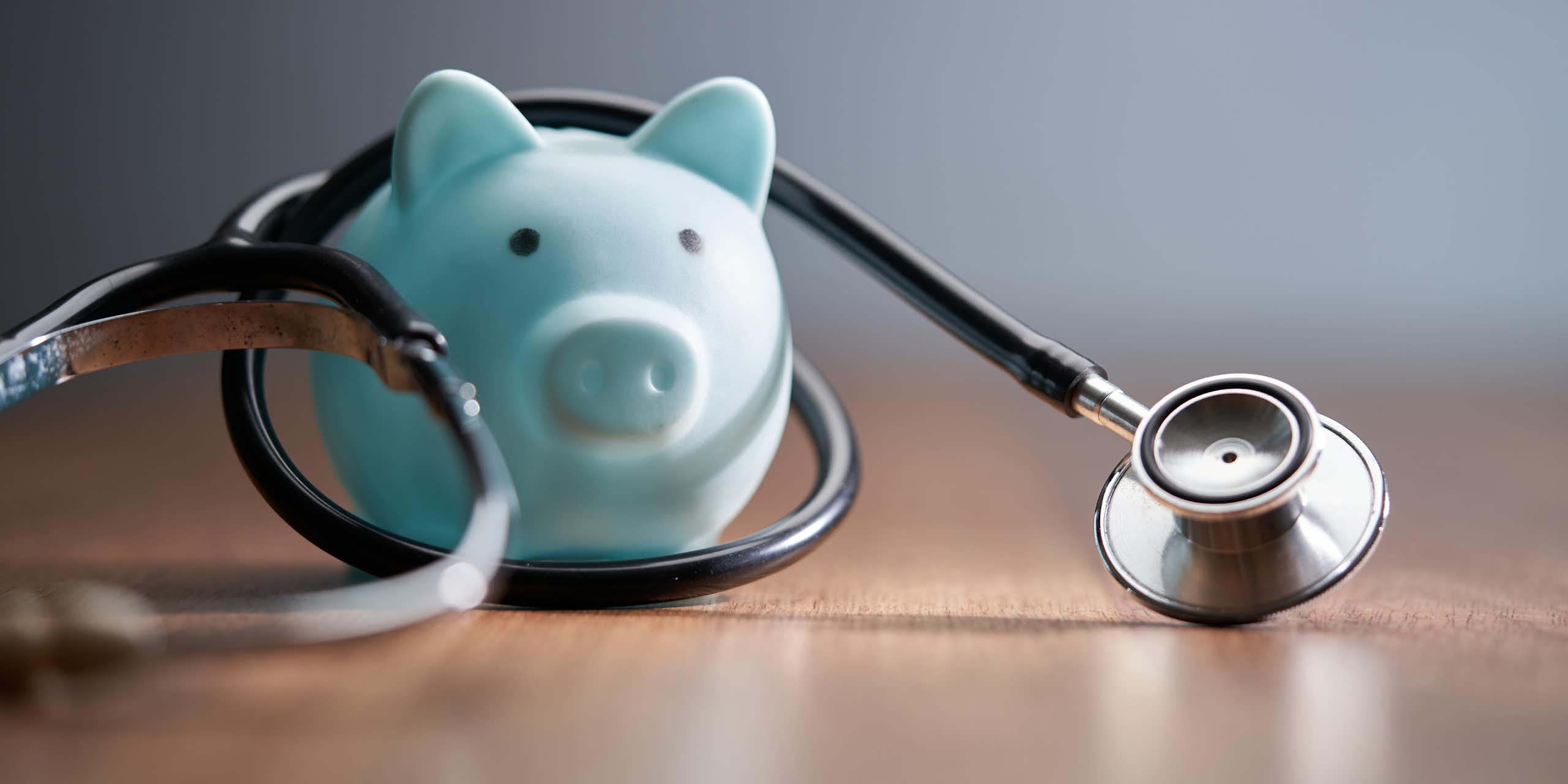 stethoscope and blue piggy bank on wood table top
