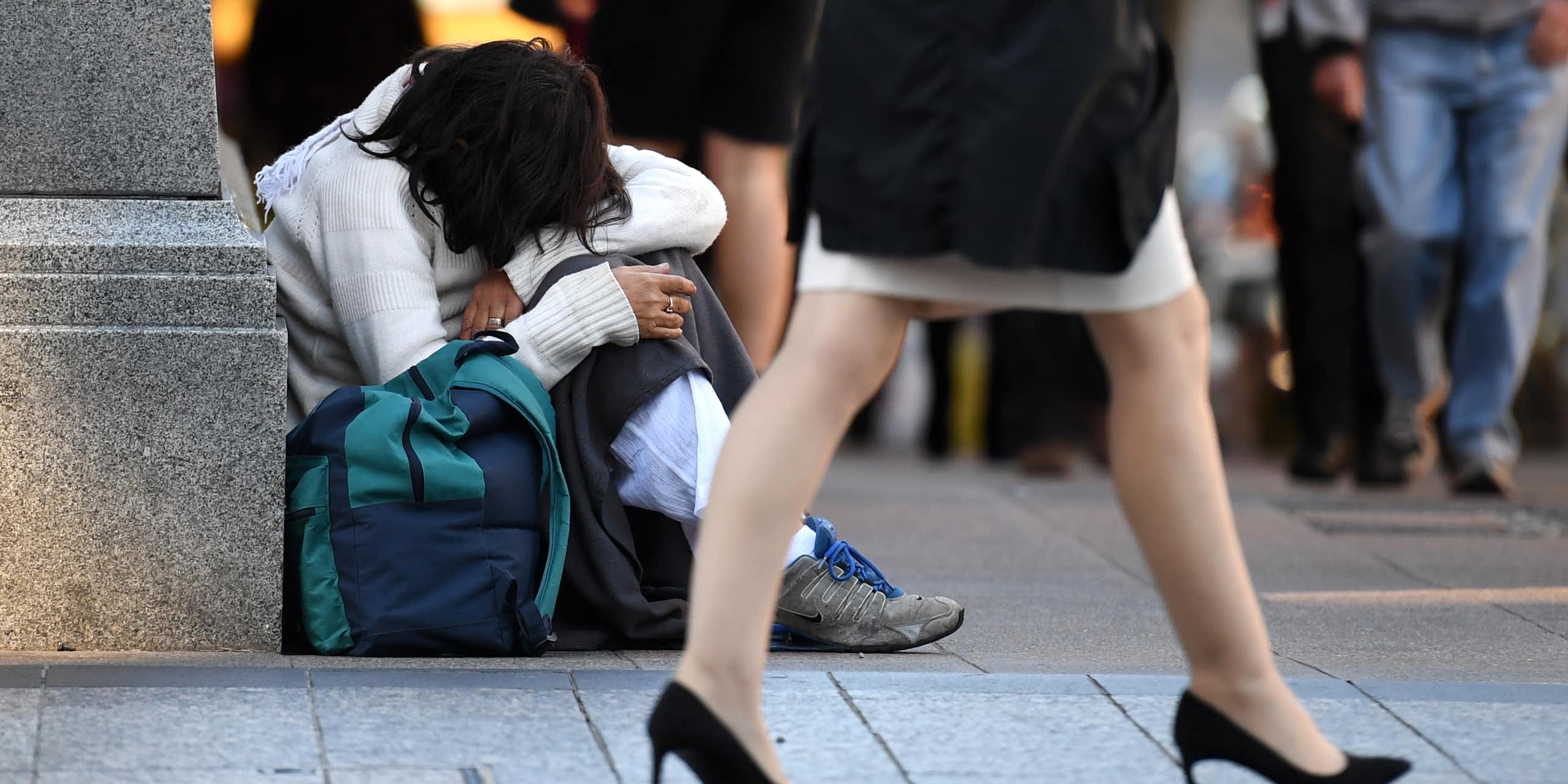 A wealthy woman walks past a homeless person on an Australian street.