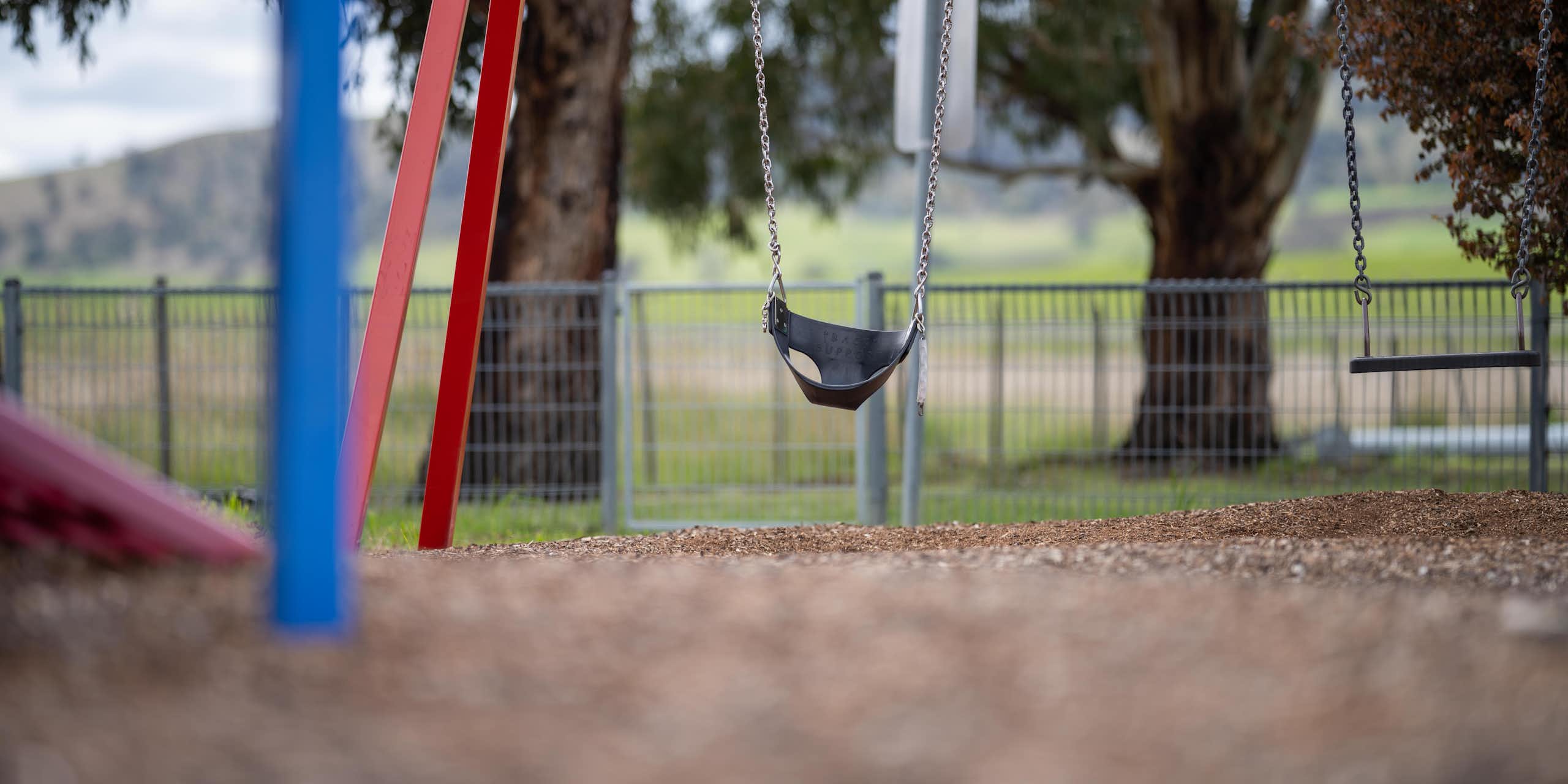 An empty swing set with trees and grass in the background.