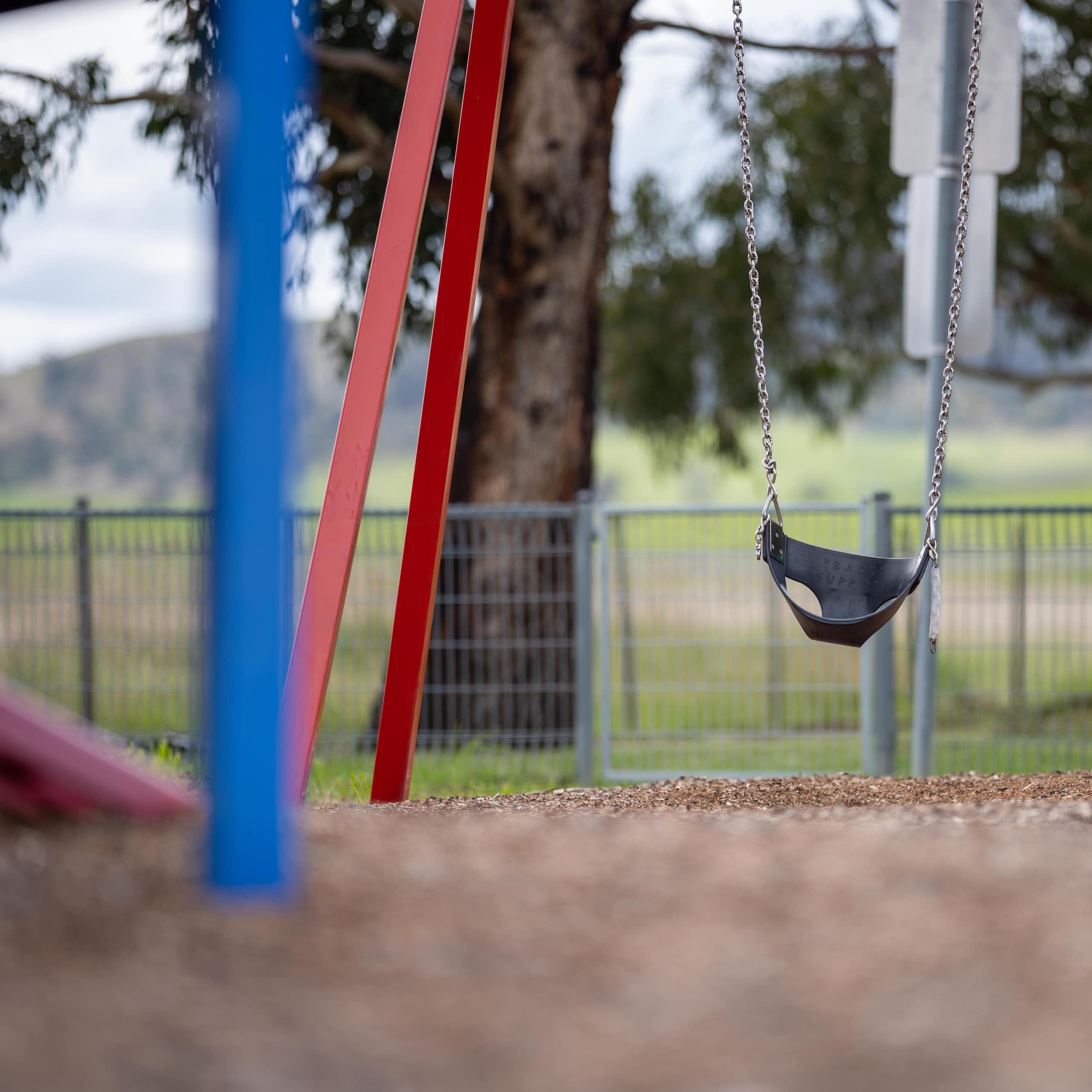 An empty swing set with trees and grass in the background.