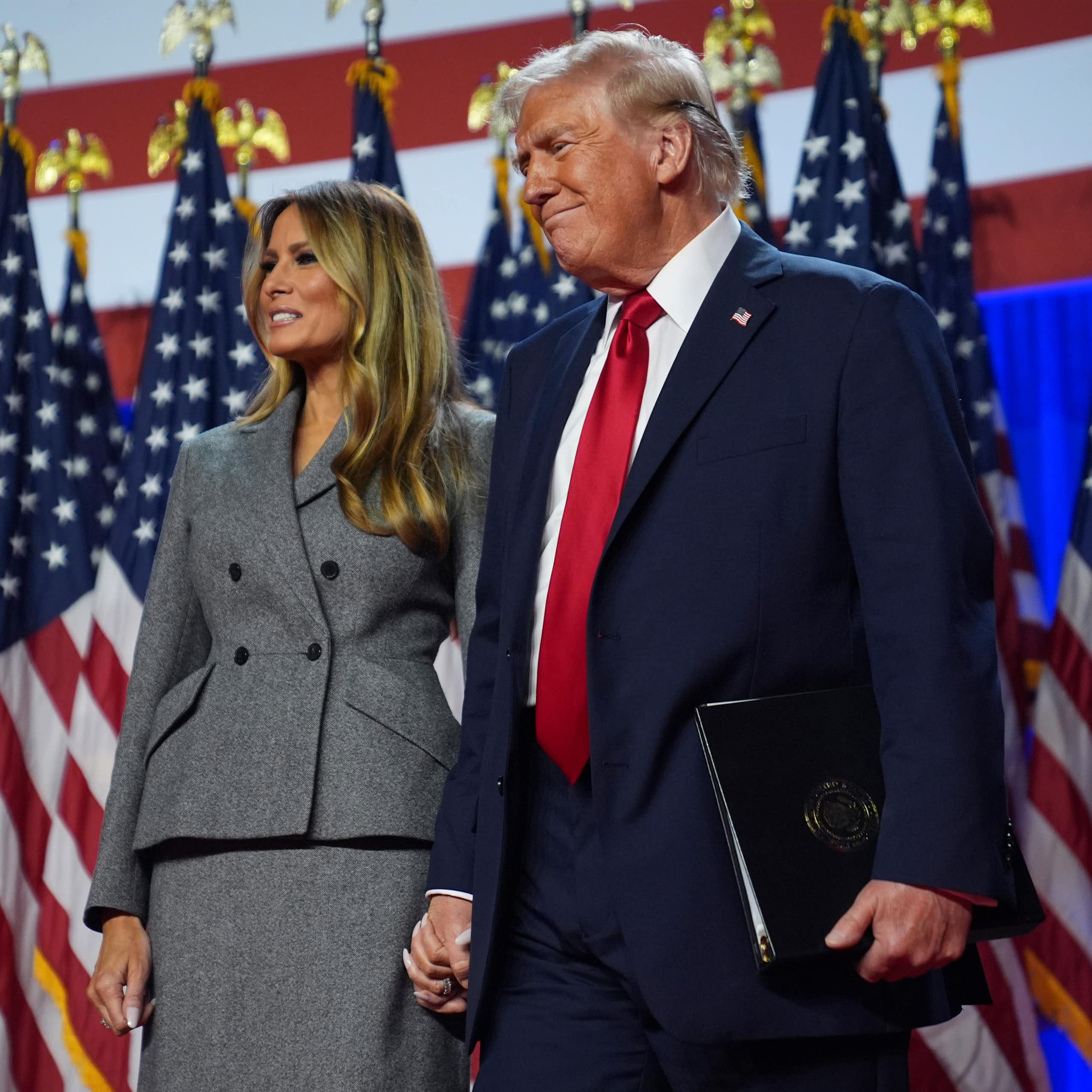 Donald and Melania Trump standing in front of US flags