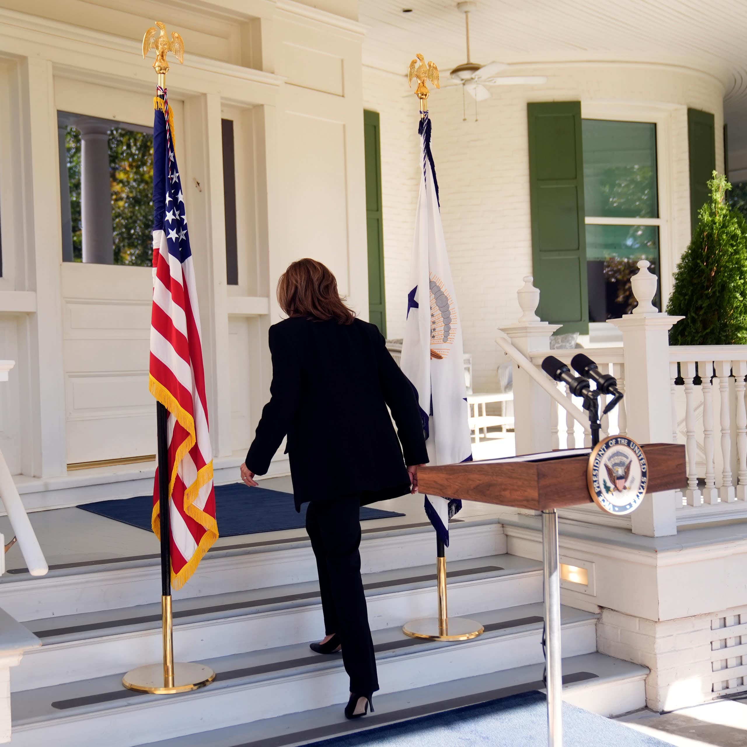 A dark-haired woman walks away from a lectern with her back to the camera.