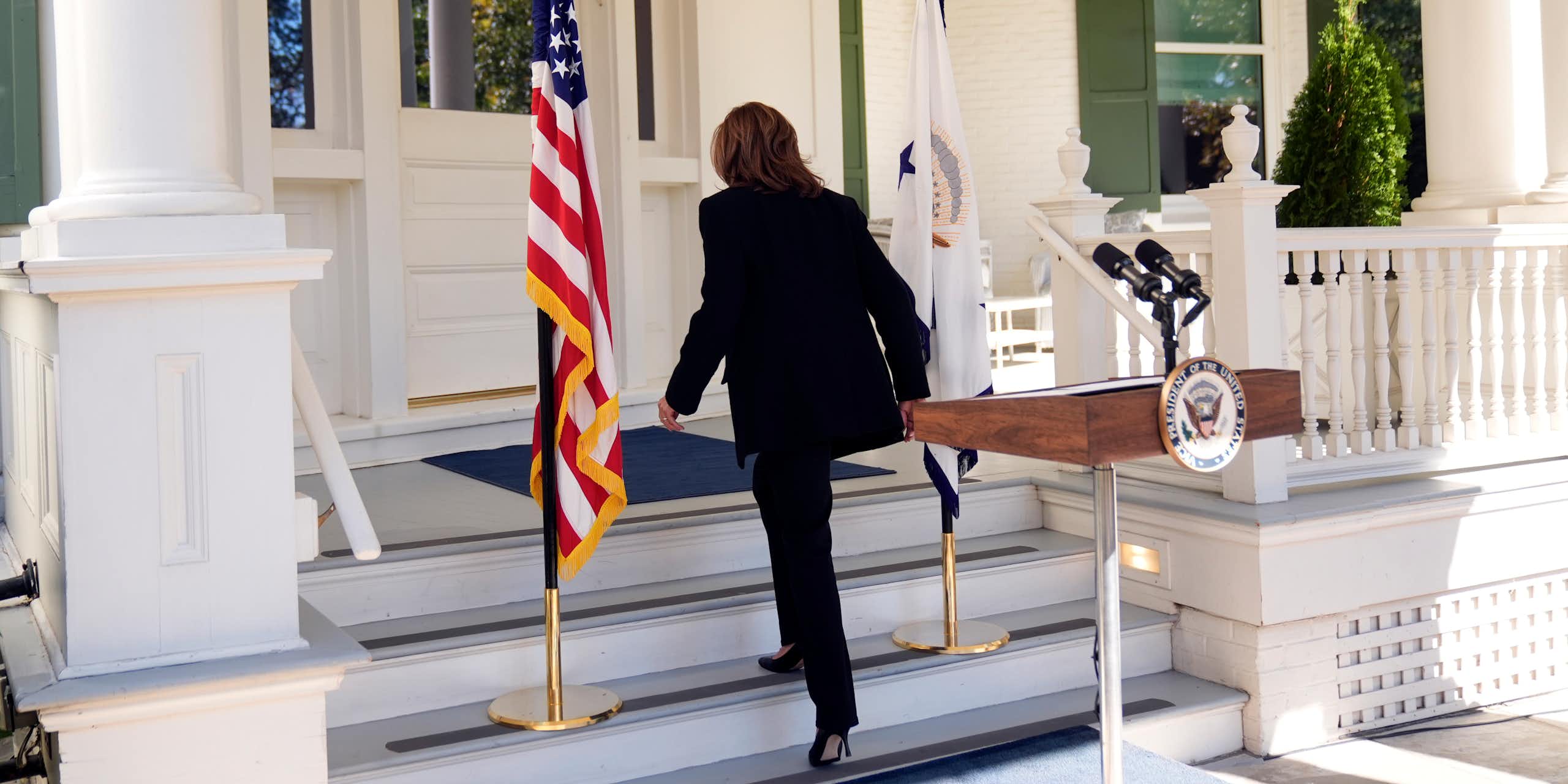 A dark-haired woman walks away from a lectern with her back to the camera.