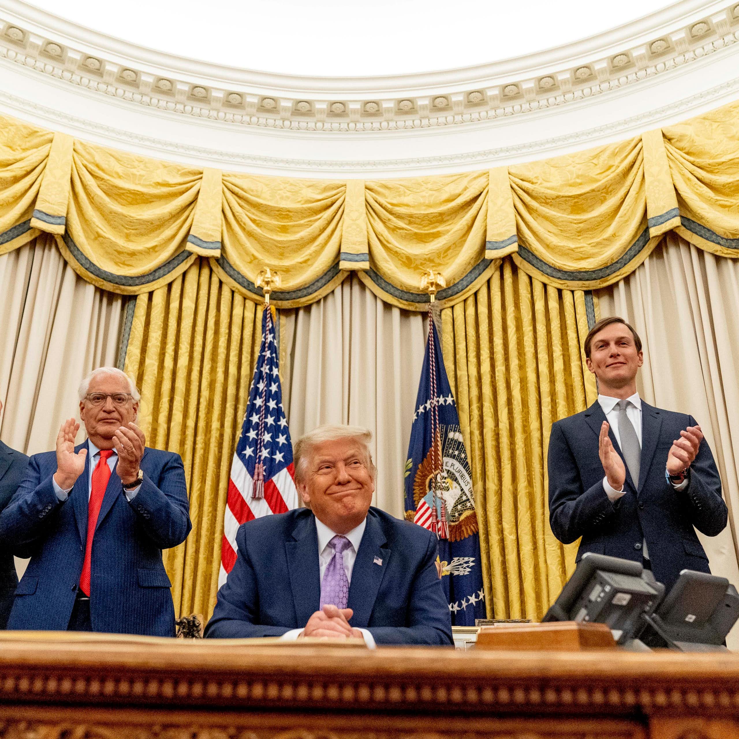 Trump sits in the Oval Office surrounded by men in suits