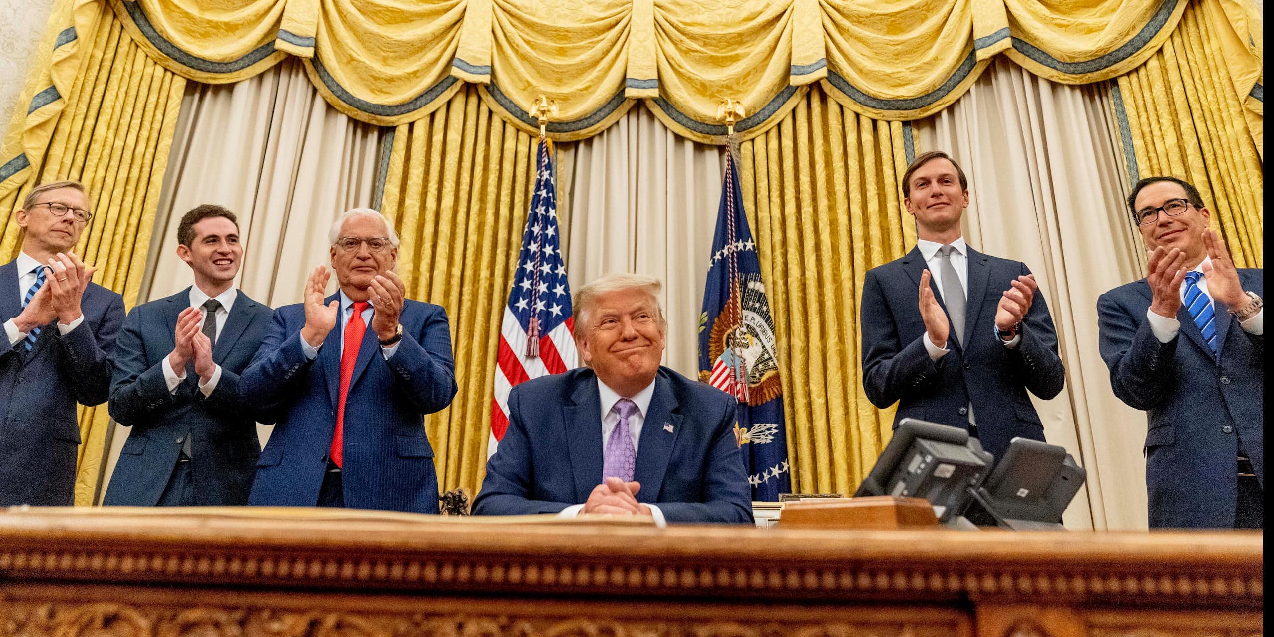 Trump sits in the Oval Office surrounded by men in suits