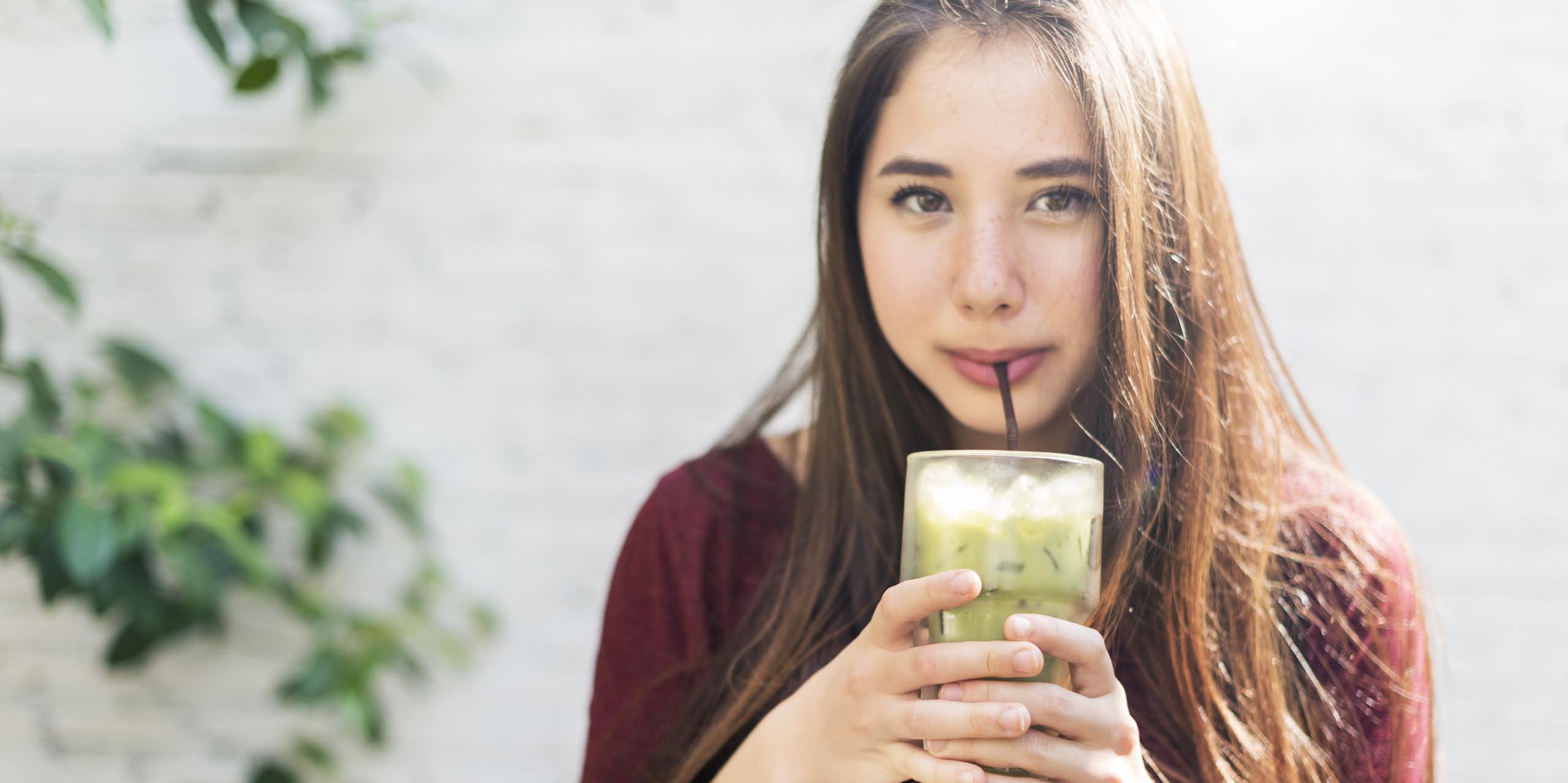 A young woman drinking an iced matcha.