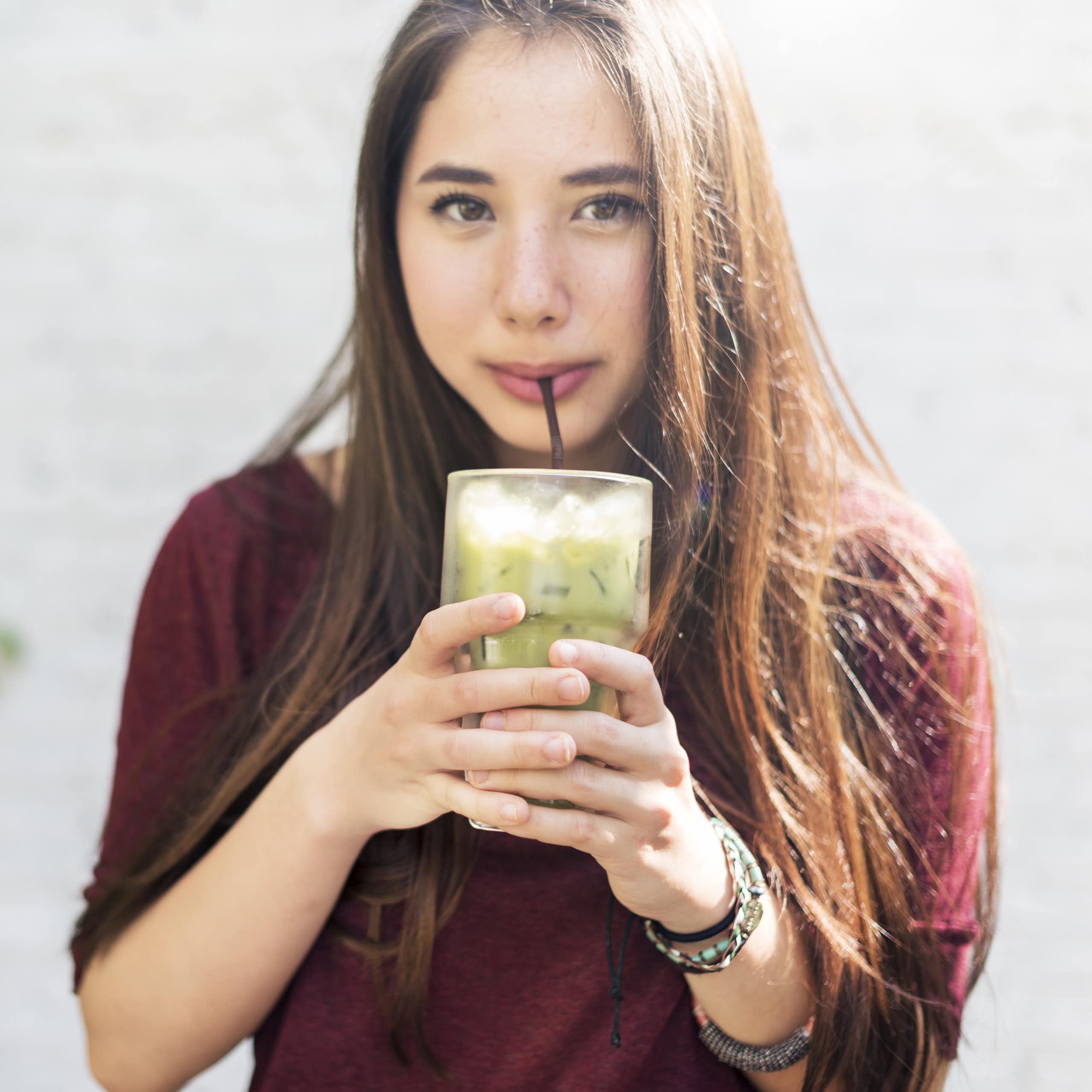 A young woman drinking an iced matcha.